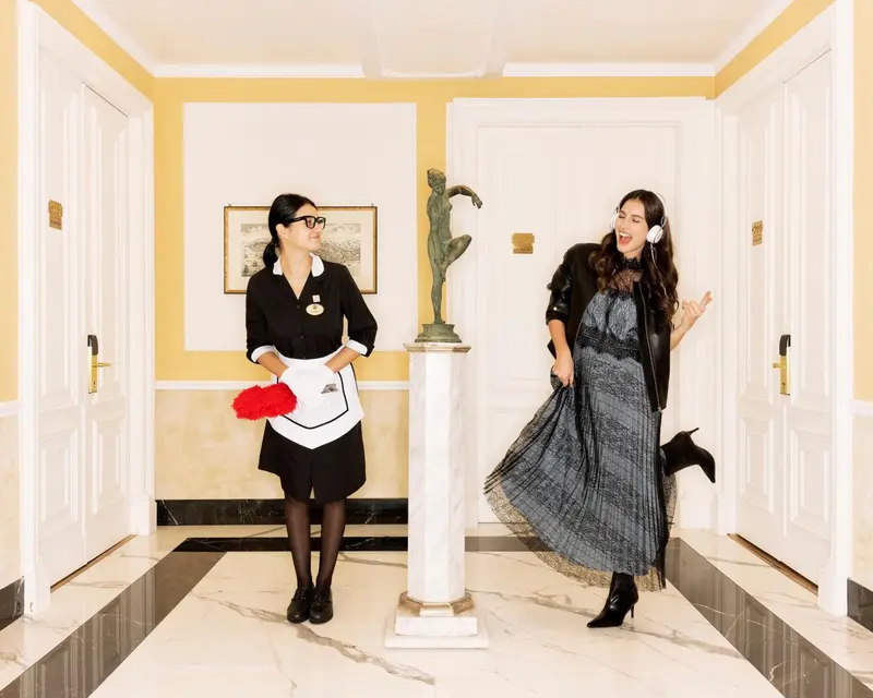 Deux femmes se tiennent dans un couloir d'hôtel décoré d'une statue et de motifs muraux.