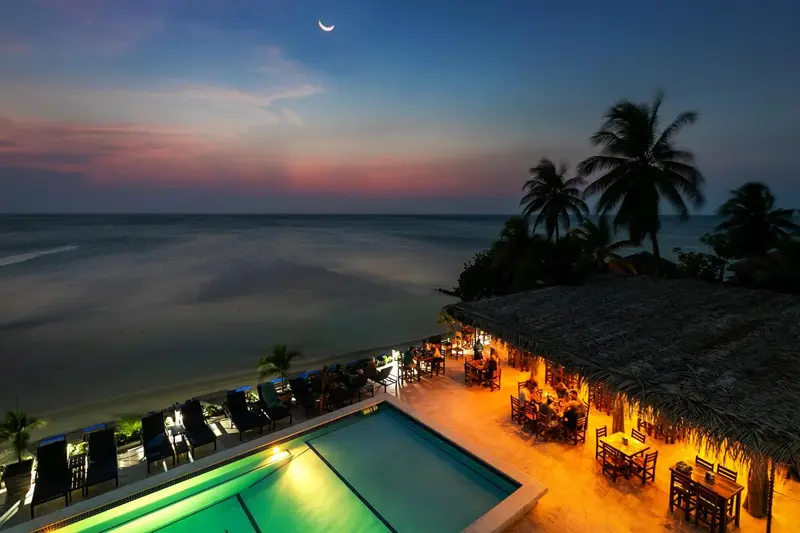 Une piscine illuminée surplombe une plage au coucher du soleil.