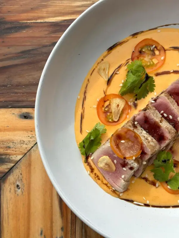 Assiette de poisson servi dans une sauce orangée, décorée d'herbes et d'épices.