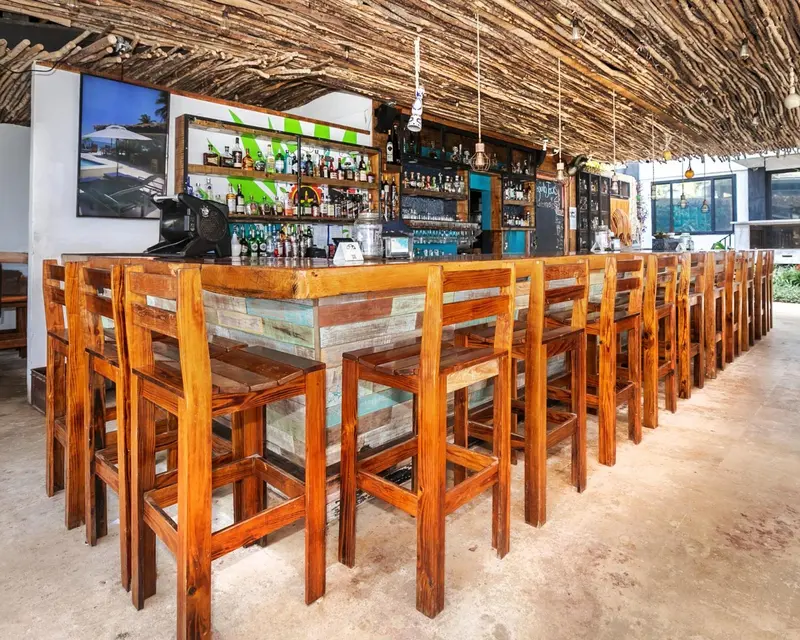 Un long comptoir de bar en bois avec des tabourets, sous un toit de chaume.