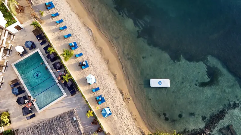 Vue aérienne d'une plage avec des transats bleus et une piscine rectangulaire.
