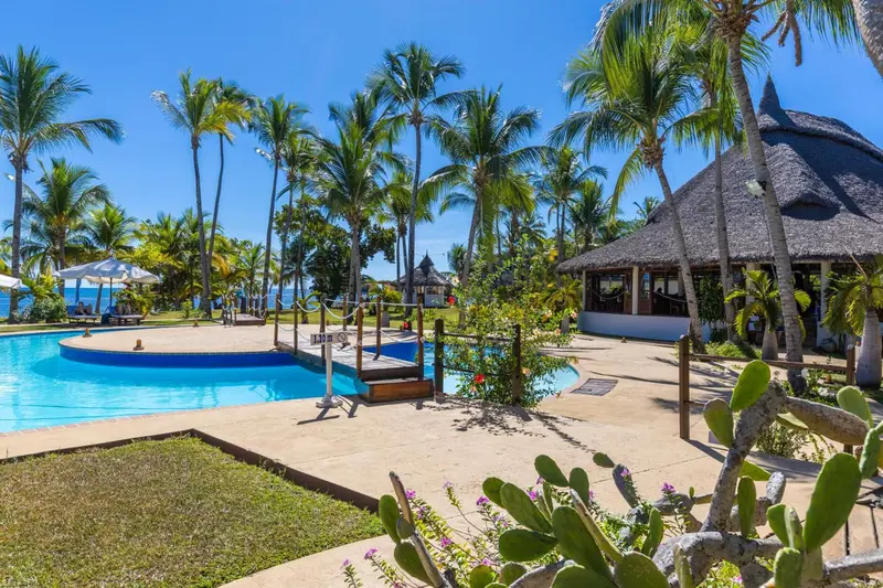 Piscine turquoise bordée d'une terrasse ensoleillée avec végétation tropicale.