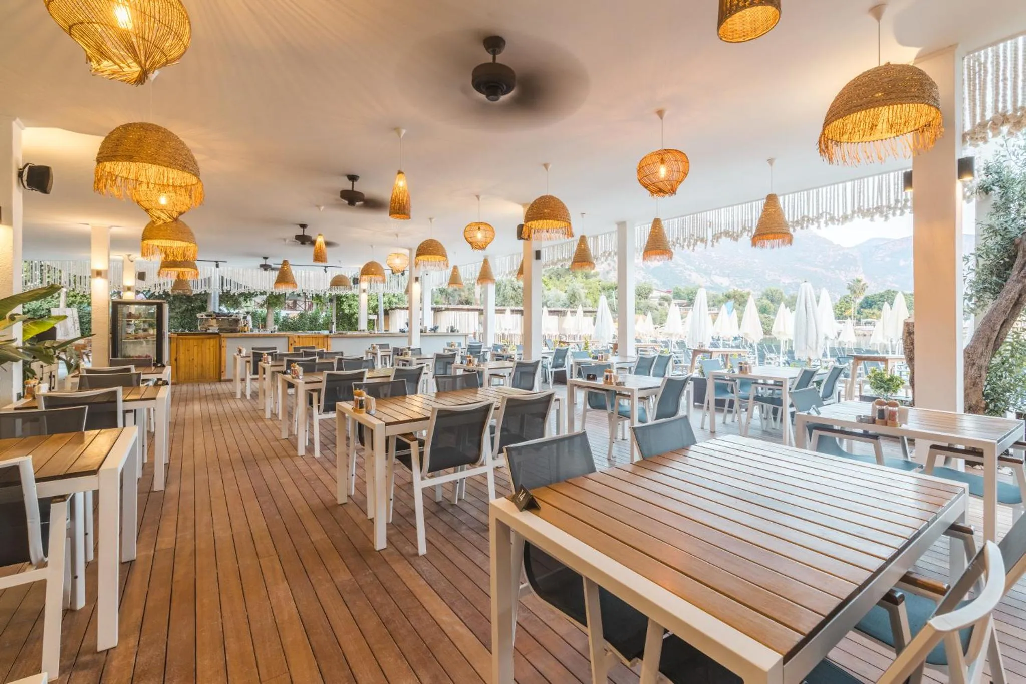 Terrasse ombragée avec tables et chaises en bois, vue sur la mer.