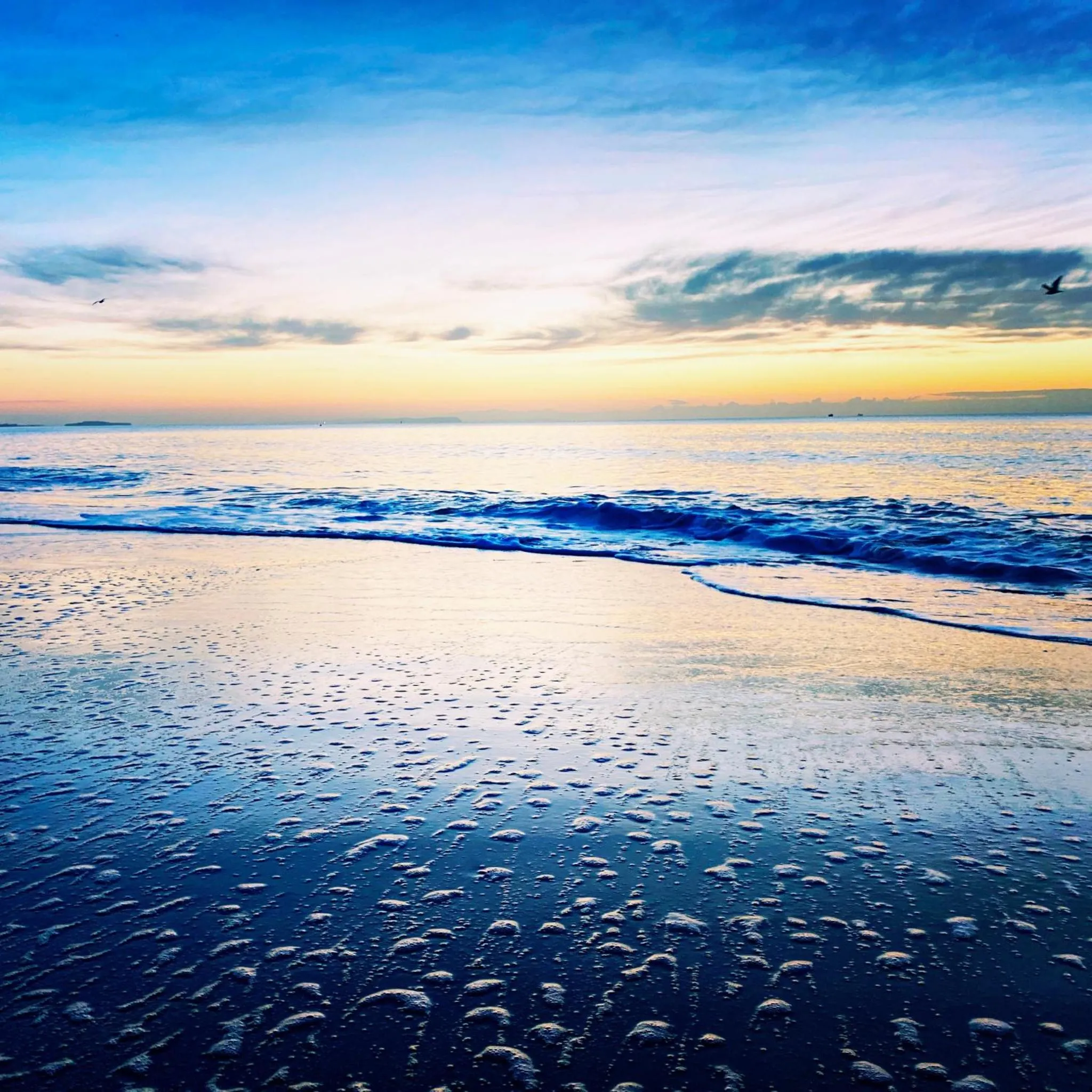 Vague déferlant sur une plage de sable au coucher du soleil.