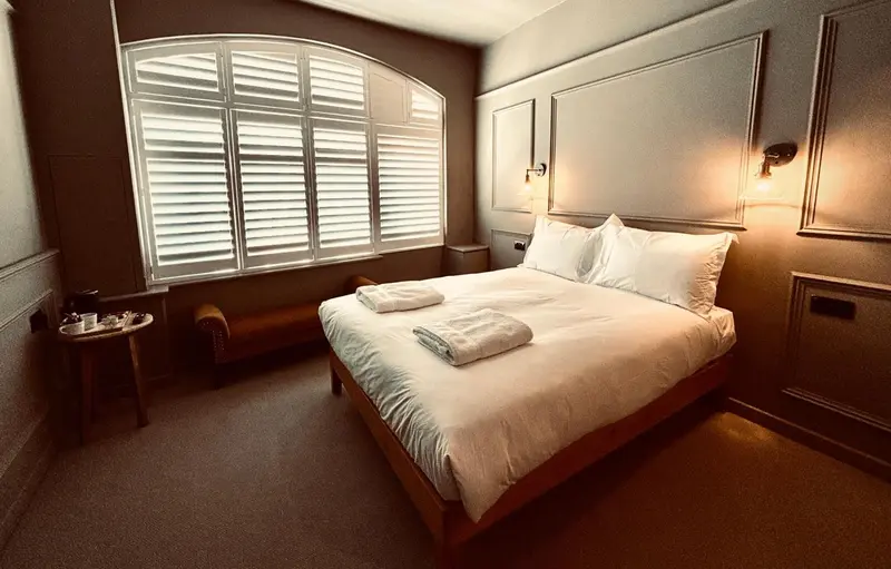 Une chambre lumineuse avec un lit recouvert d'une couverture blanche et un fauteuil près de la fenêtre.
