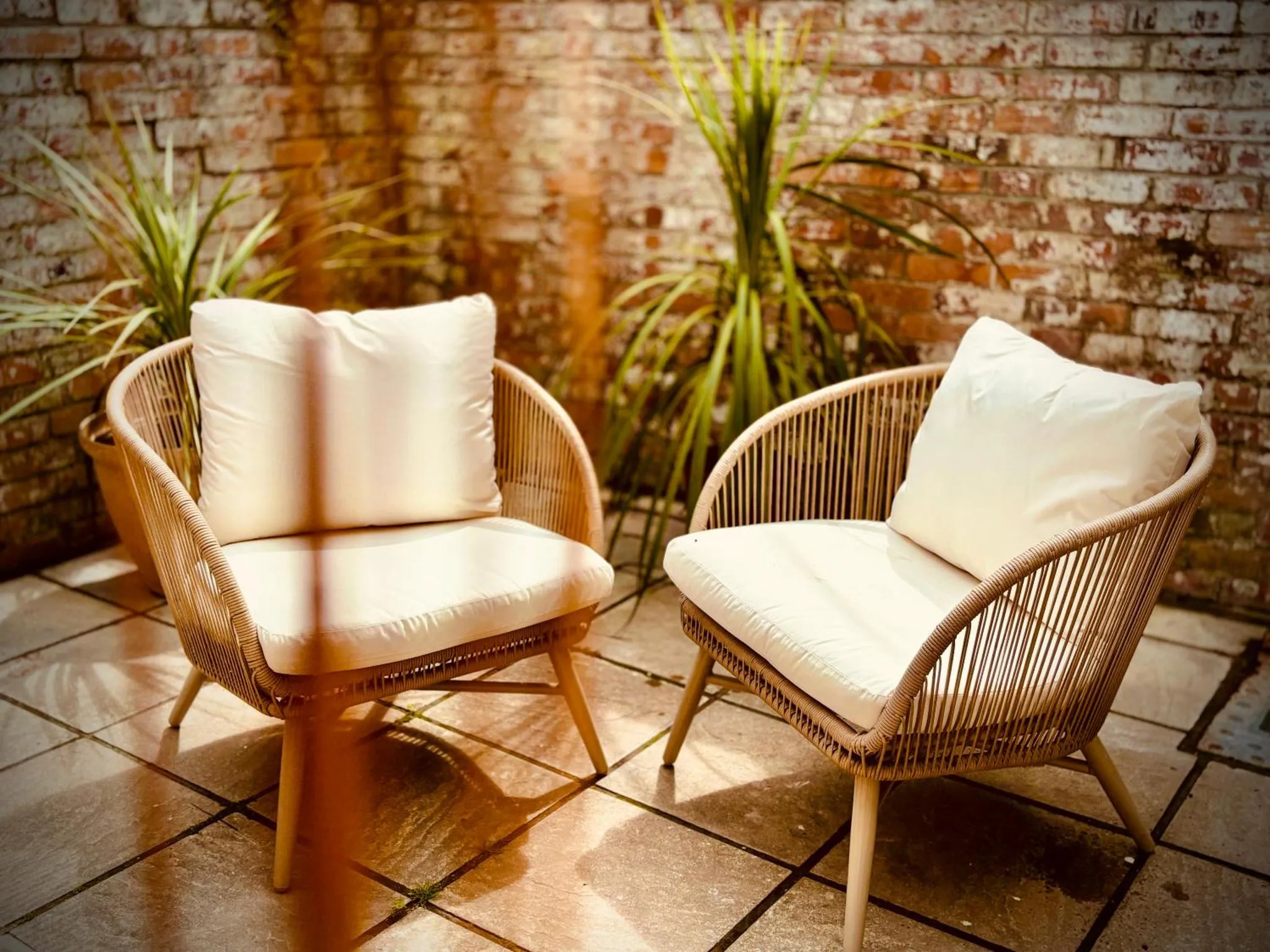 Deux fauteuils en rotin avec coussins sur une terrasse carrelée.