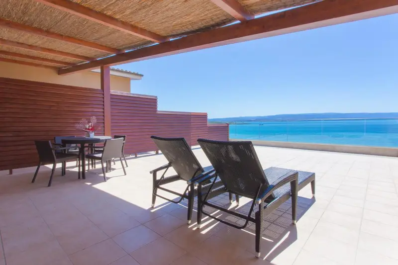 Terrasse aménagée avec transats et table basse donnant sur la mer.