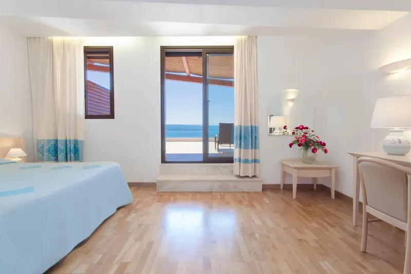 Chambre lumineuse avec un lit fait et une vue sur la mer par une grande baie vitrée.