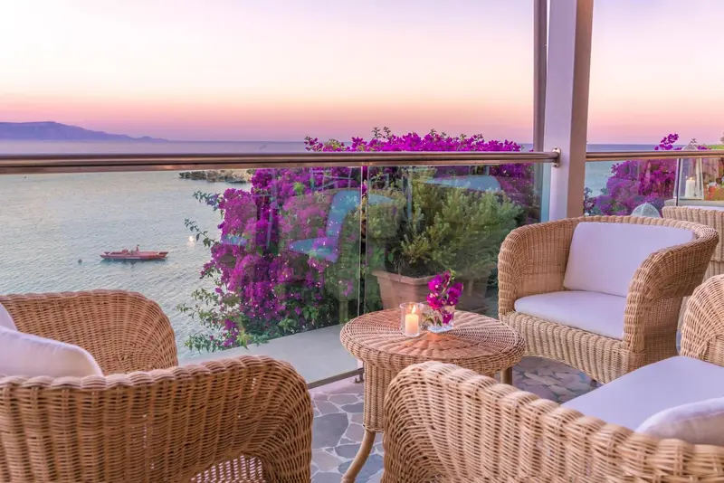 Terrasse avec mobilier en rotin donnant sur la mer au coucher du soleil.