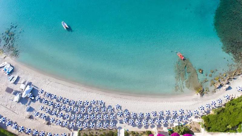 Vue aérienne d'une plage de sable blanc bordée d'une eau turquoise et de transats bleus.