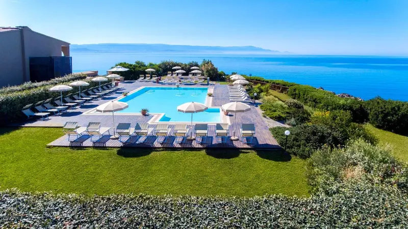 Piscine rectangulaire avec transats et parasols, surplombant la mer et les montagnes.