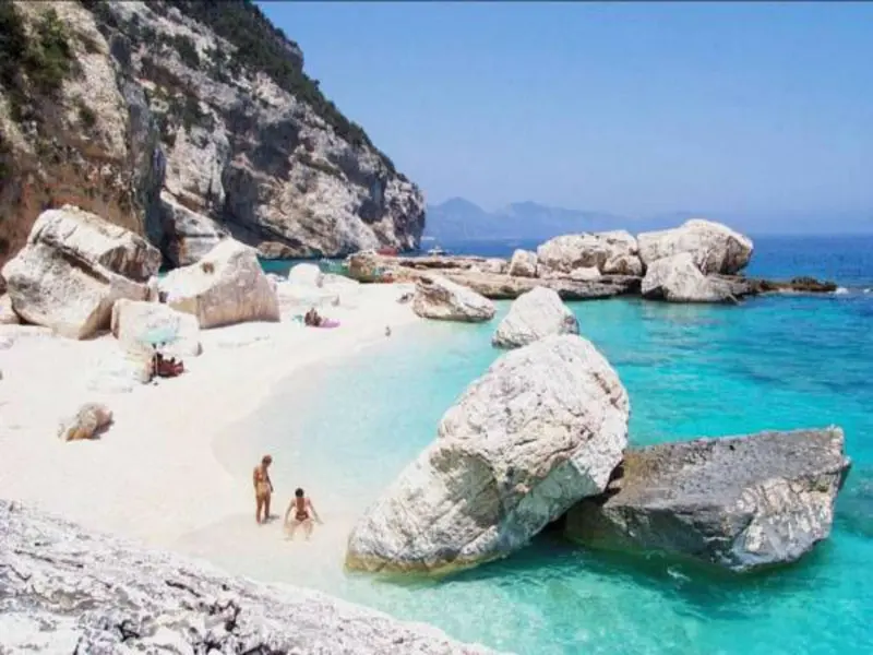 Une plage de sable blanc bordée de rochers et baignée par une eau turquoise.