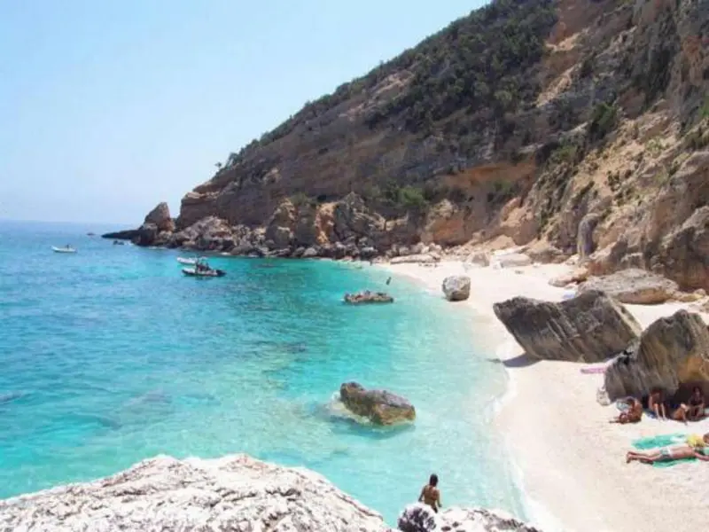 Une plage de sable blanc bordée d'une eau turquoise et de rochers.