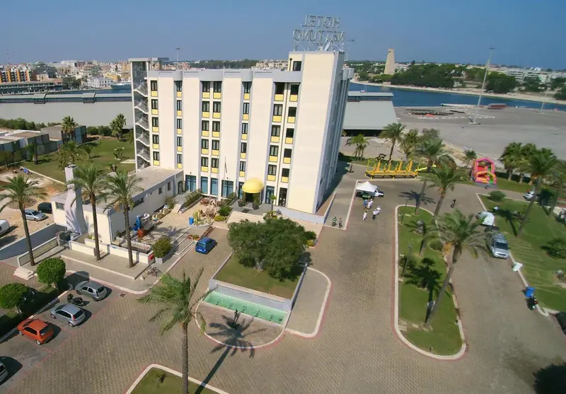 Vue aérienne d'un bâtiment blanc avec des balcons, entouré de végétation et d'une zone pavée.