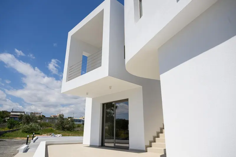 Architecture moderne blanche avec des lignes épurées et une végétation verdoyante en arrière-plan.
