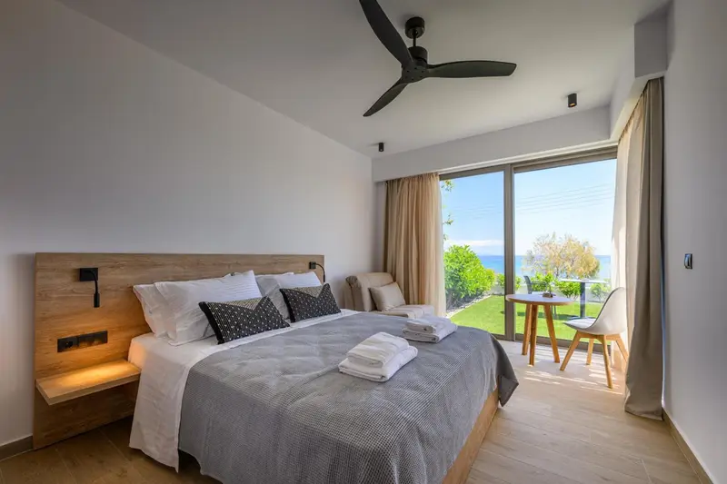 Une chambre lumineuse avec un grand lit et un coin salon donnant sur une vue mer.