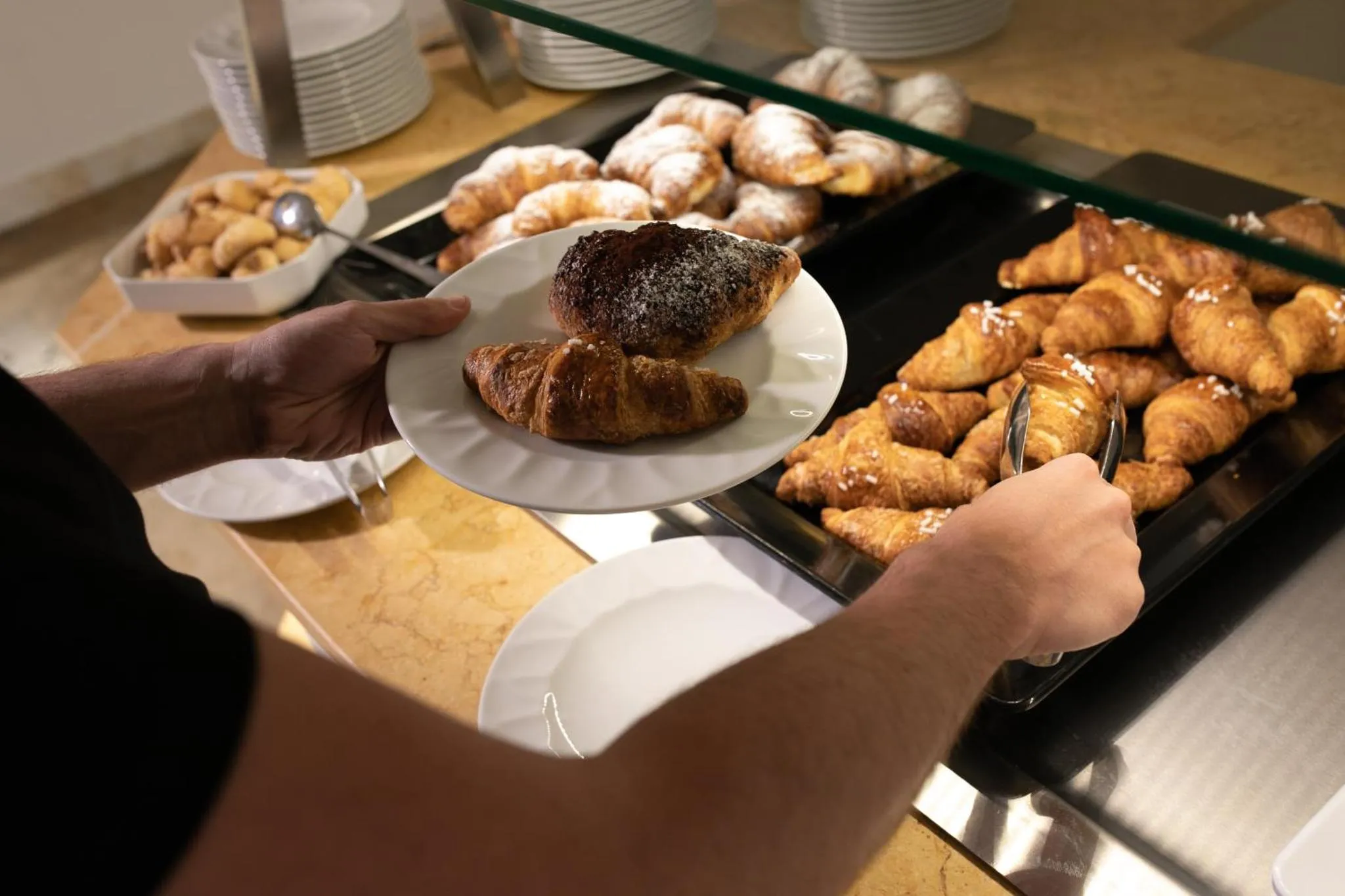 Une main prend un croissant sur un buffet de viennoiseries.