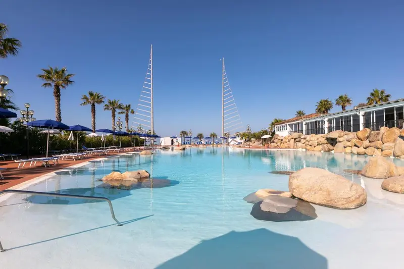 Une piscine turquoise avec des rochers et des transats sous des parasols.