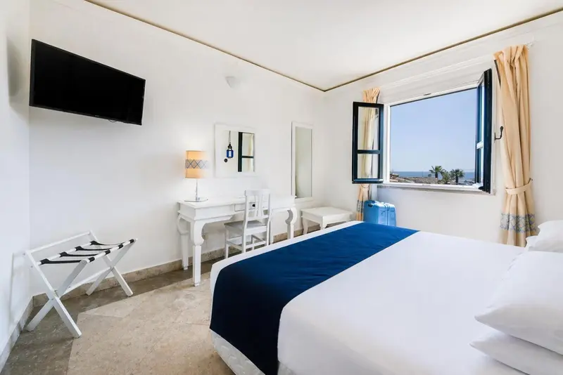 Une chambre lumineuse avec un lit recouvert d'une couverture bleue et une fenêtre donnant sur la mer.