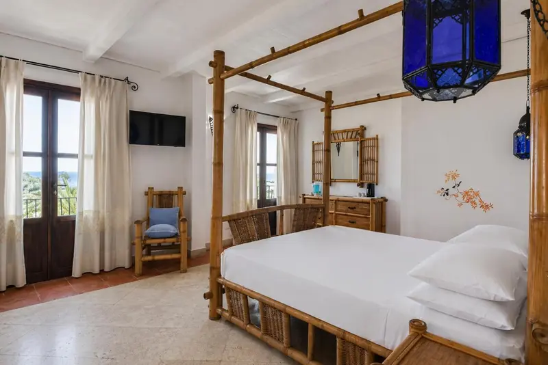 Chambre lumineuse avec lit à baldaquin et vue sur la mer.