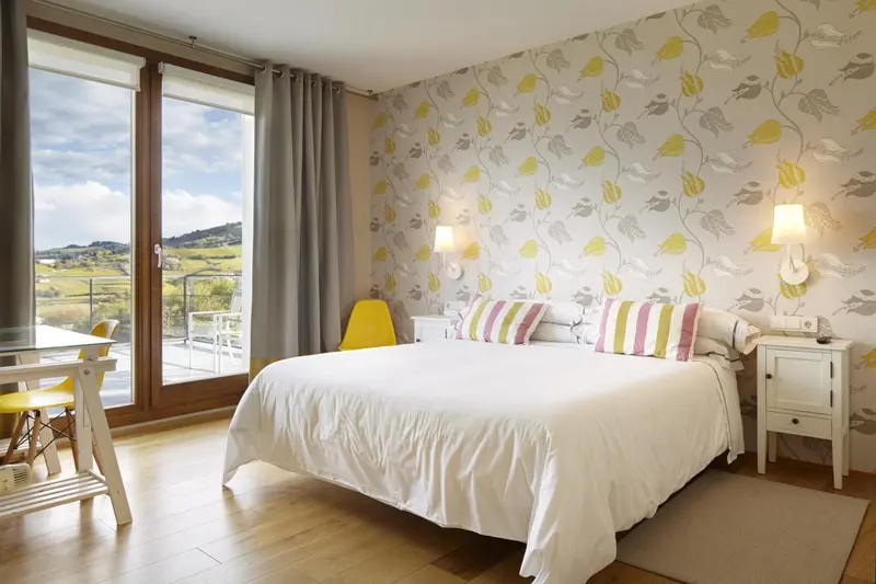 Une chambre lumineuse avec un lit blanc et une vue sur un paysage montagneux.