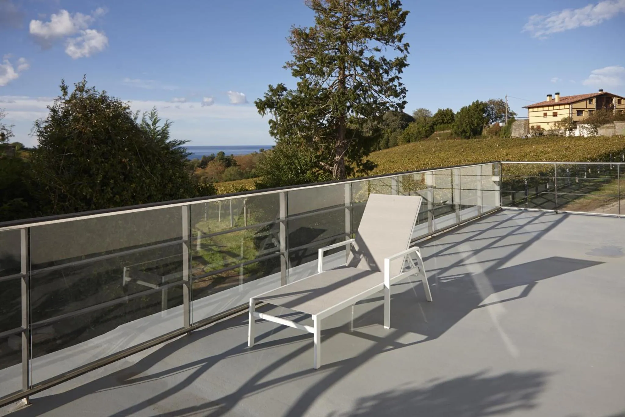 Une terrasse moderne avec un transat offre une vue sur la mer et la végétation environnante.