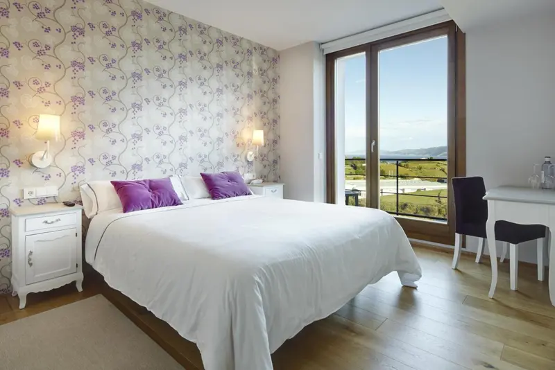 Une chambre lumineuse avec un grand lit et une vue sur un paysage verdoyant.