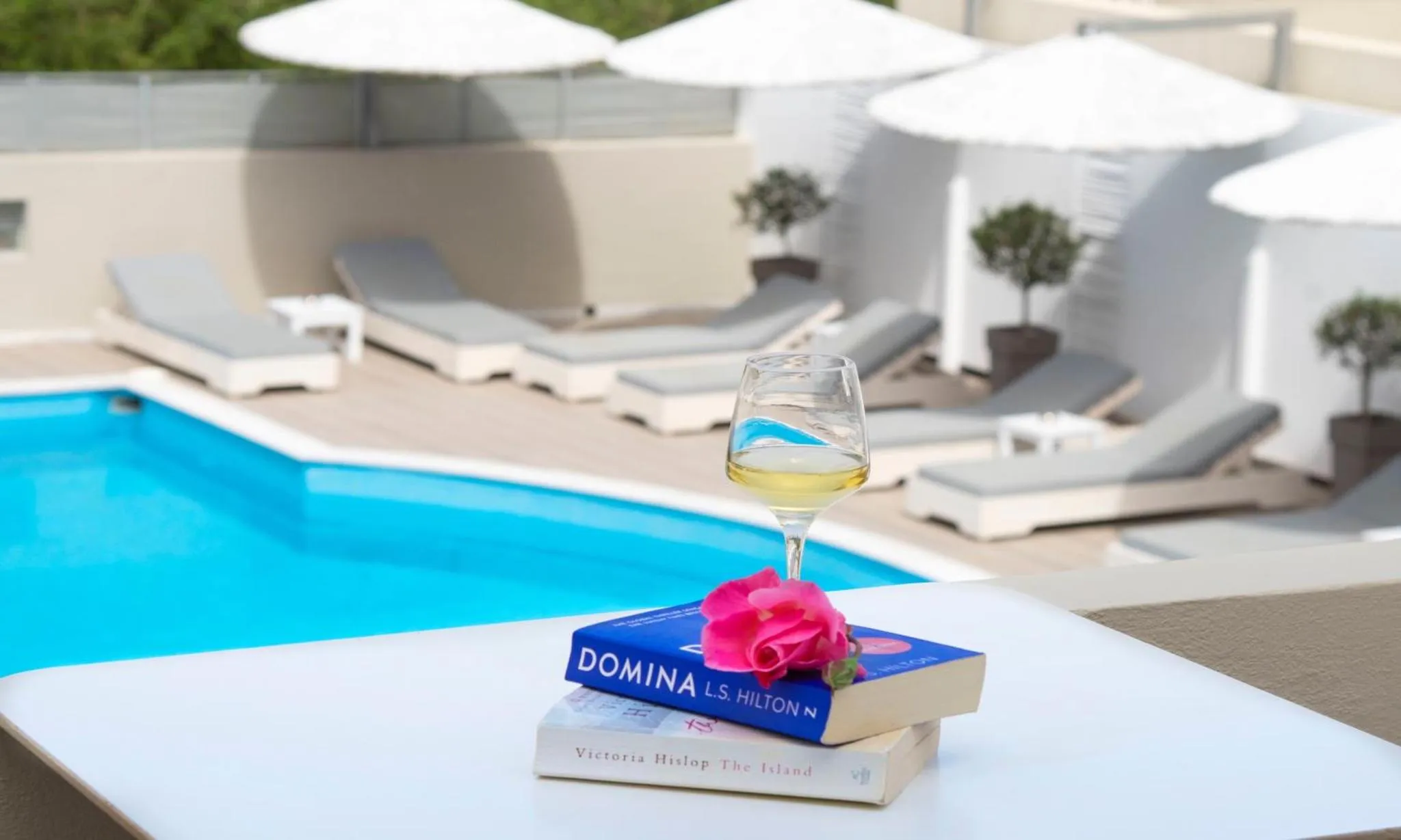 Un verre de vin et des livres reposent sur une table au bord d'une piscine ensoleillée.