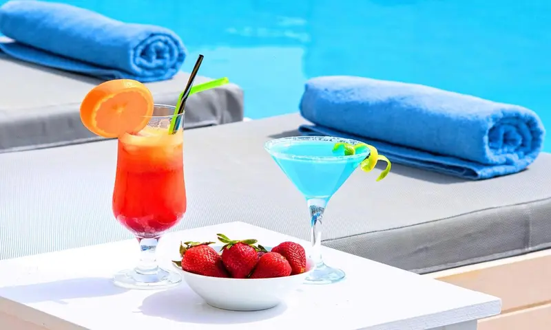 Des cocktails colorés et des fruits frais sont servis au bord d'une piscine.