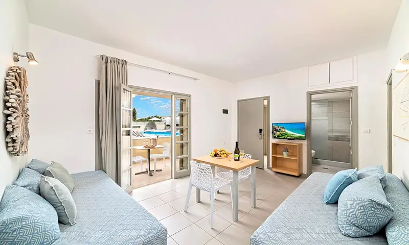Espace de vie lumineux avec canapés, table et accès à une terrasse avec vue sur une piscine.
