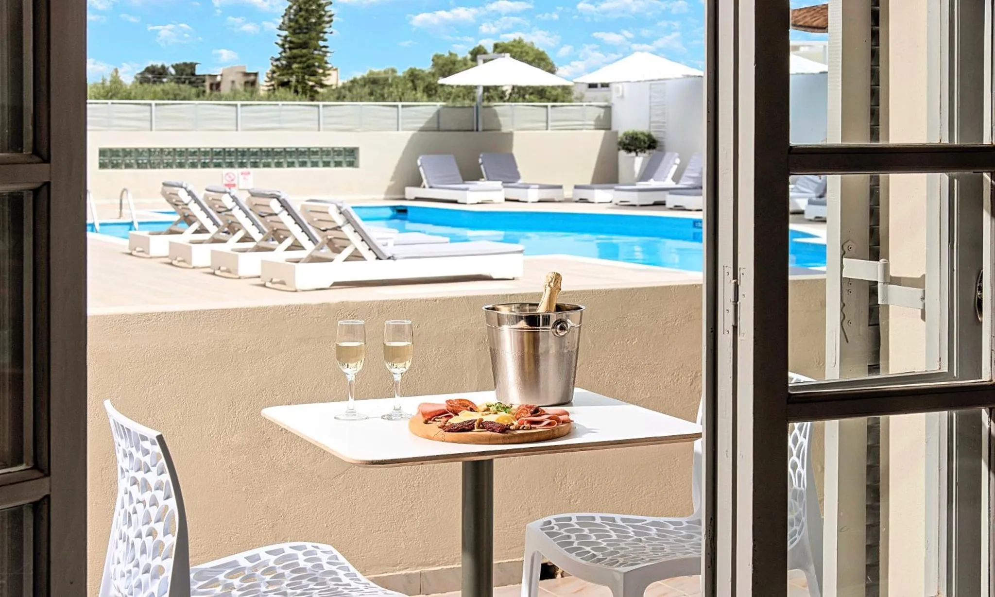 Une table avec des verres et une assiette est placée devant une piscine avec des transats.