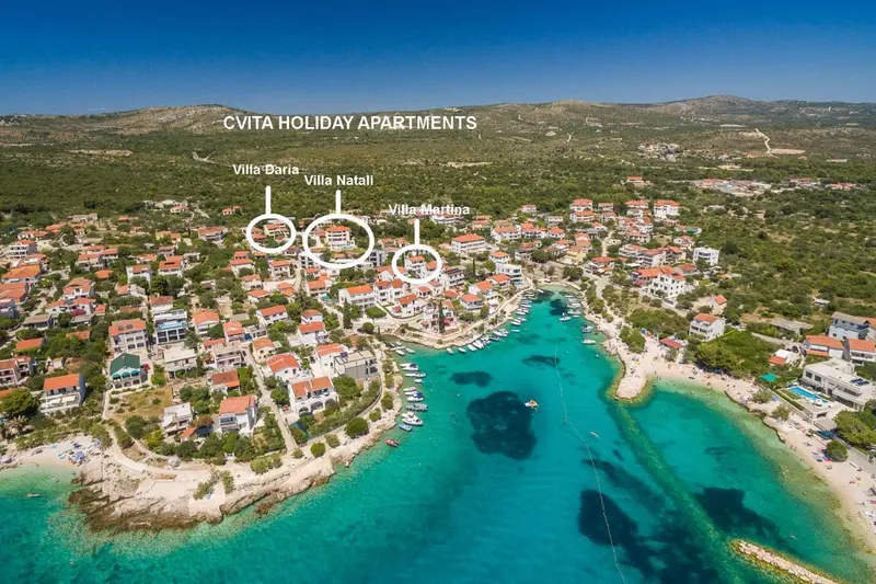 Vue aérienne d'un village côtier avec des bâtiments et une baie turquoise.