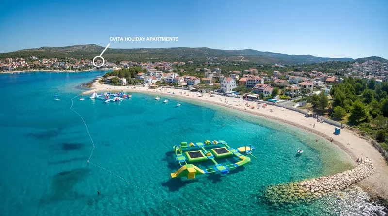 Vue aérienne d'une plage de sable fin bordée d'une eau turquoise et de quelques structures flottantes.