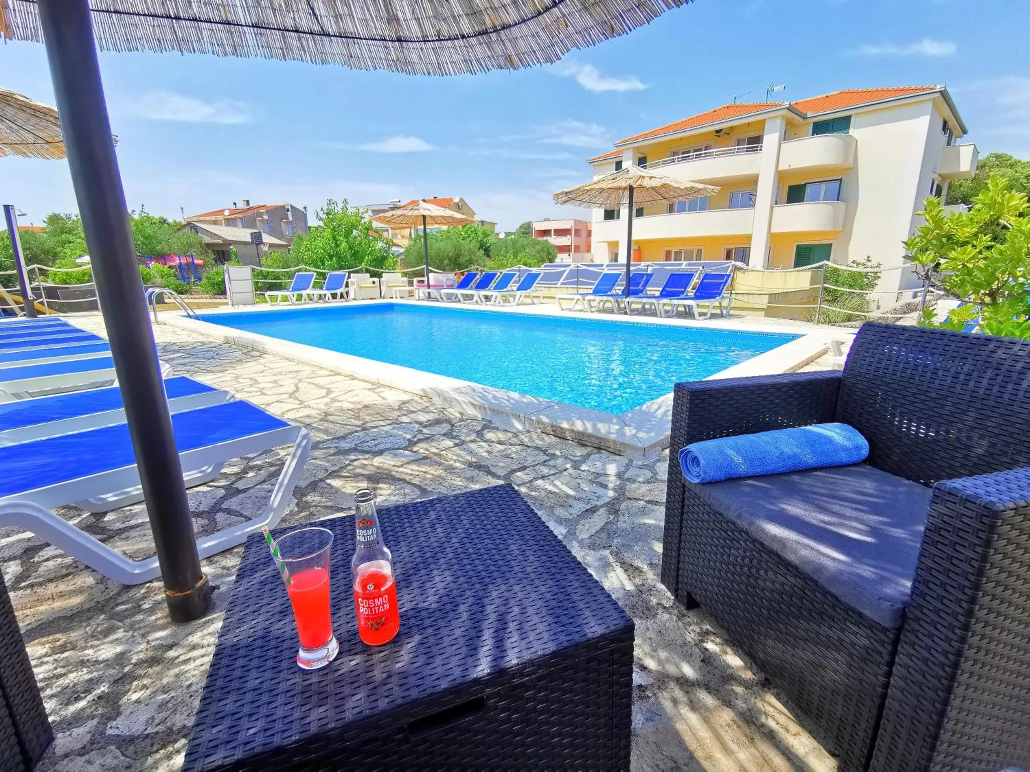 Transats et table basse avec boissons au bord d'une piscine ensoleillée.