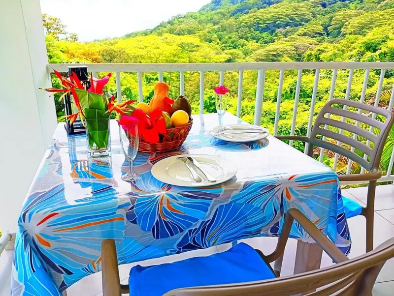 Une table dressée avec des fruits et de la vaisselle sur une terrasse ensoleillée.