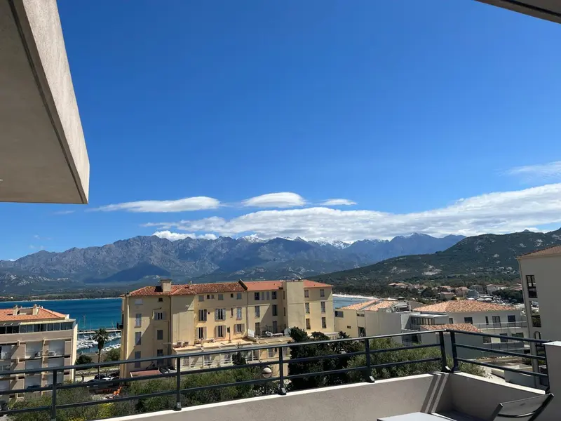 Vue dégagée sur un paysage montagneux et une ville côtière ensoleillée.