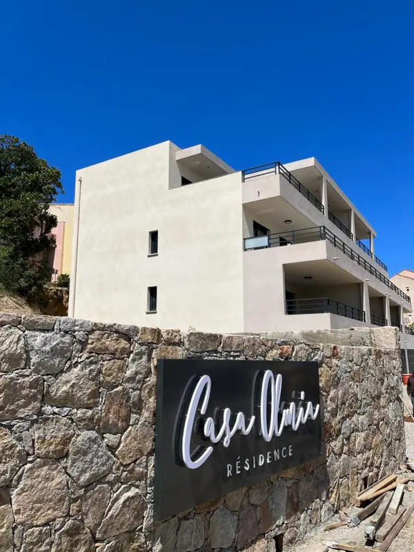 Façade d'un bâtiment blanc à plusieurs étages avec des balcons et un mur en pierre.