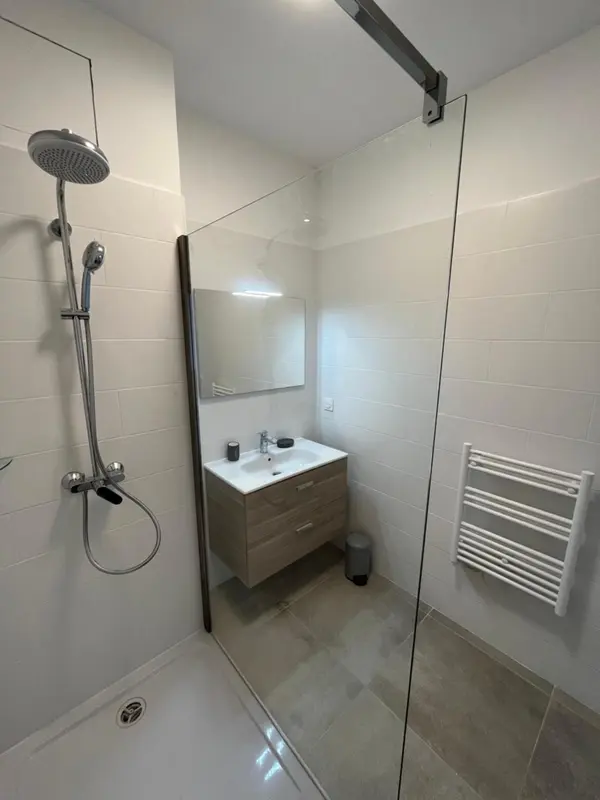 Une douche à l'italienne moderne avec des carreaux blancs et un meuble vasque en bois clair.