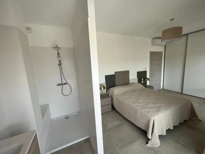 Une chambre lumineuse avec douche à l'italienne et lit recouvert d'une couverture.