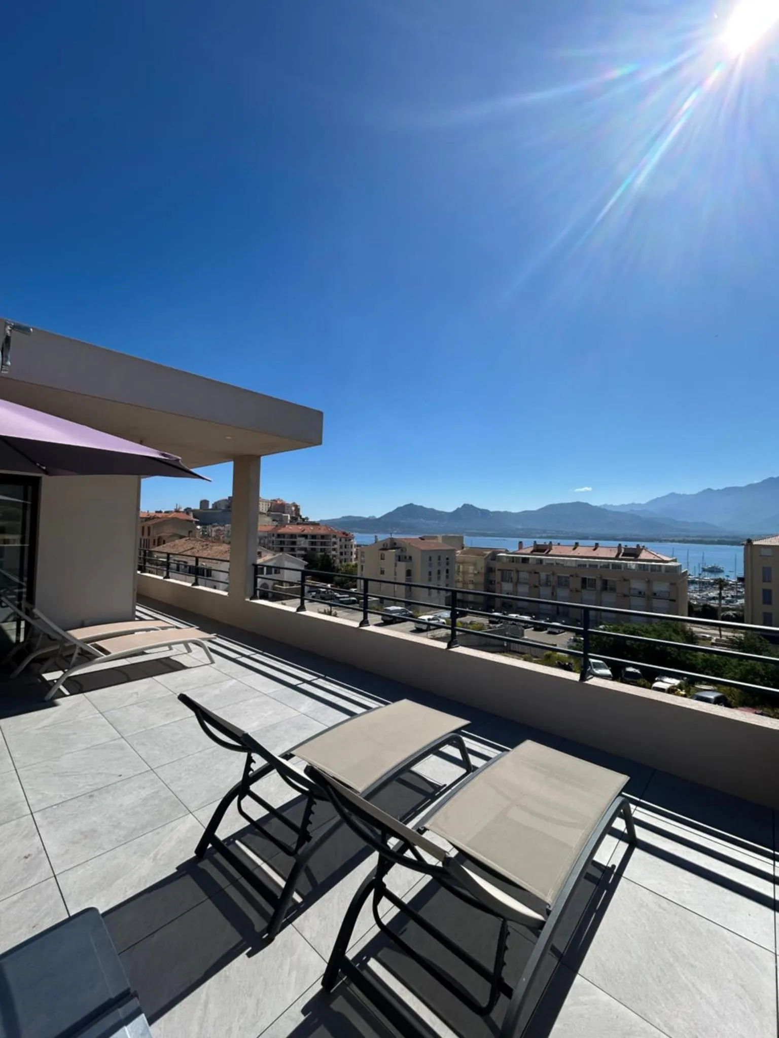 Terrasse aménagée avec chaises longues et vue sur la mer et les montagnes.
