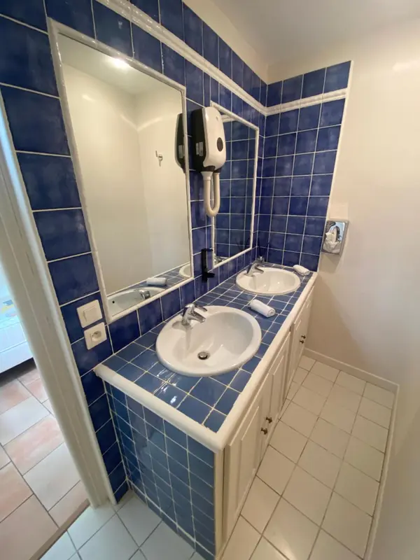 Une salle de bain carrelée avec deux lavabos et un distributeur de savon.