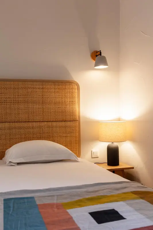 Un lit avec une tête de lit en rotin et une lampe de chevet.