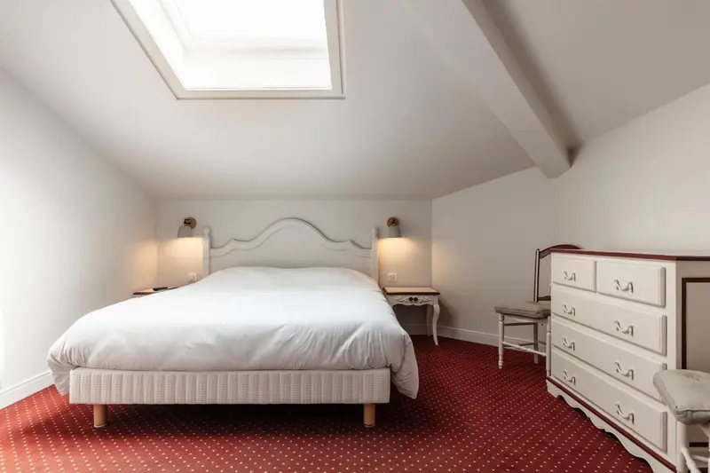 Une chambre lumineuse avec un lit blanc et des meubles en bois.