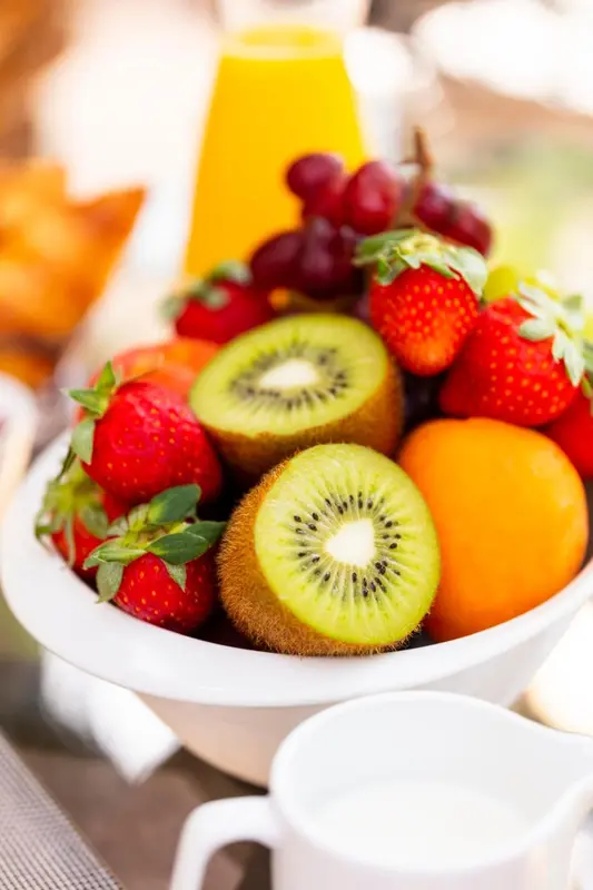 Assortiment de fruits frais et de viennoiseries présentés dans un saladier blanc.