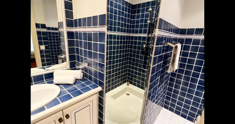 Une salle de bain carrelée de bleu avec douche et lavabo.