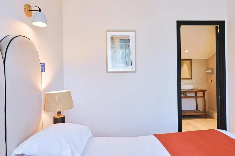 Une chambre lumineuse avec un lit simple et un accès à une salle de bain.
