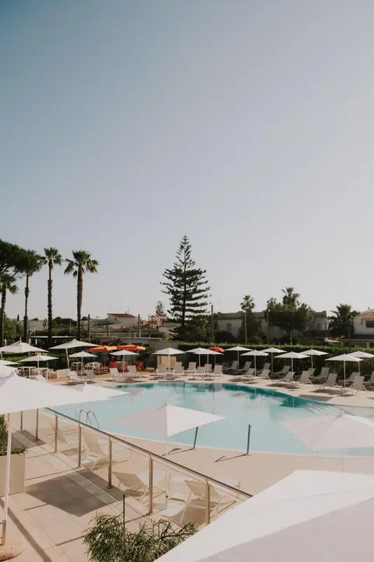 Piscine ensoleillée avec transats blancs et parasols.