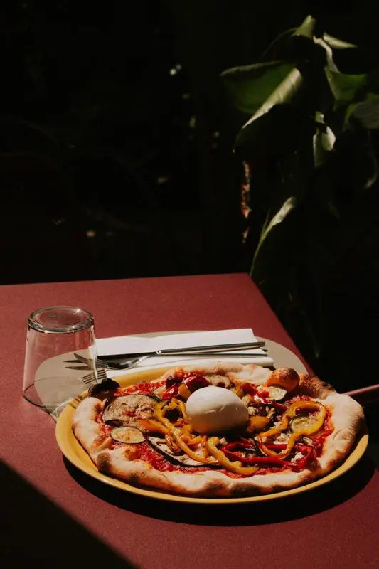 Une pizza colorée est présentée sur une table rouge avec des couverts.