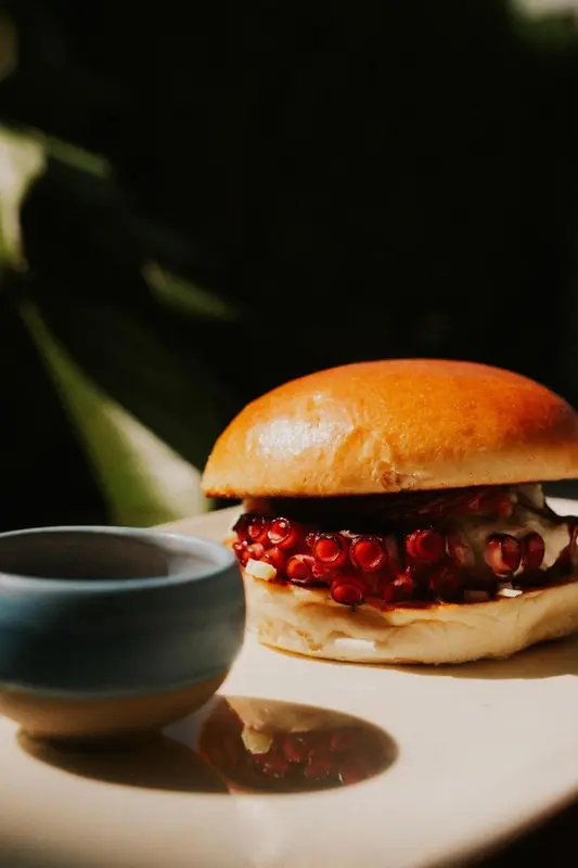 Un hamburger garni de graines de grenade est servi avec une sauce dans un bol.