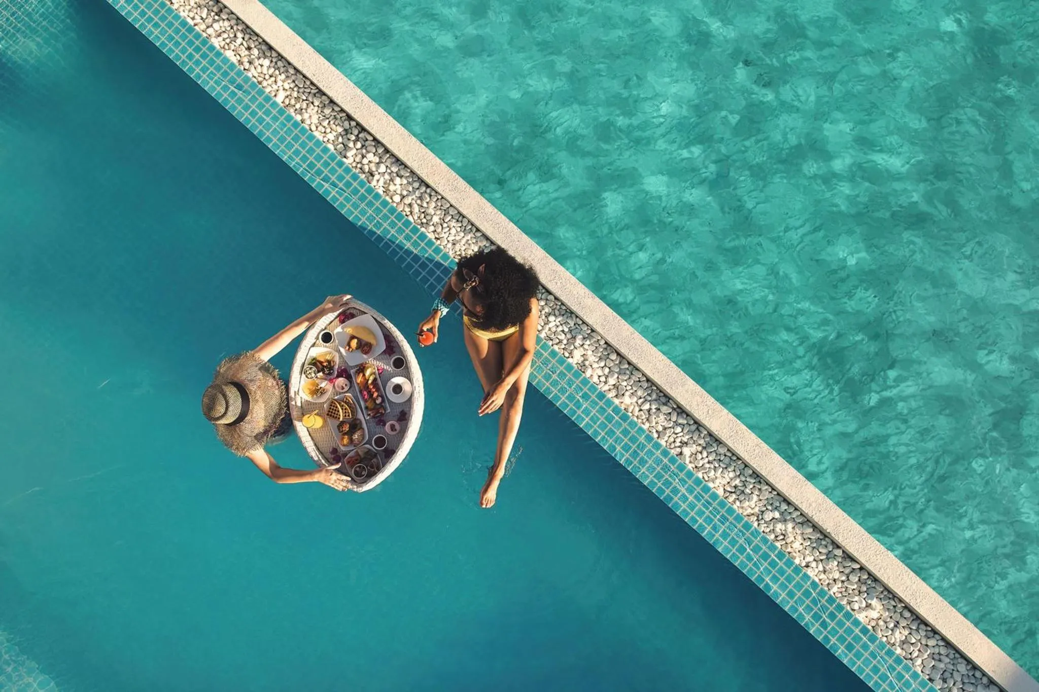 Deux personnes se détendent au bord d'une piscine avec des plateaux de nourriture et de boissons.